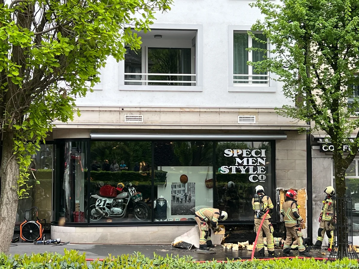Man sieht Feuerwehrleute vor einem Haus mit Schaufenster.